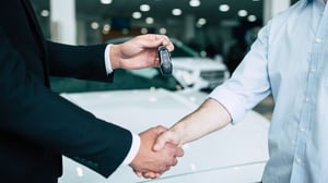 two men shaking hands while one hands over car keys